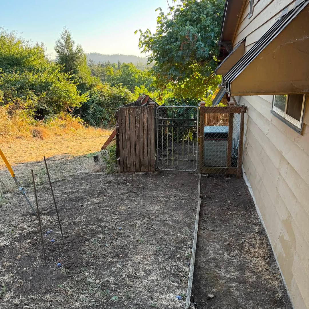 Cleared dirt along a house wall, fence, and metal gate